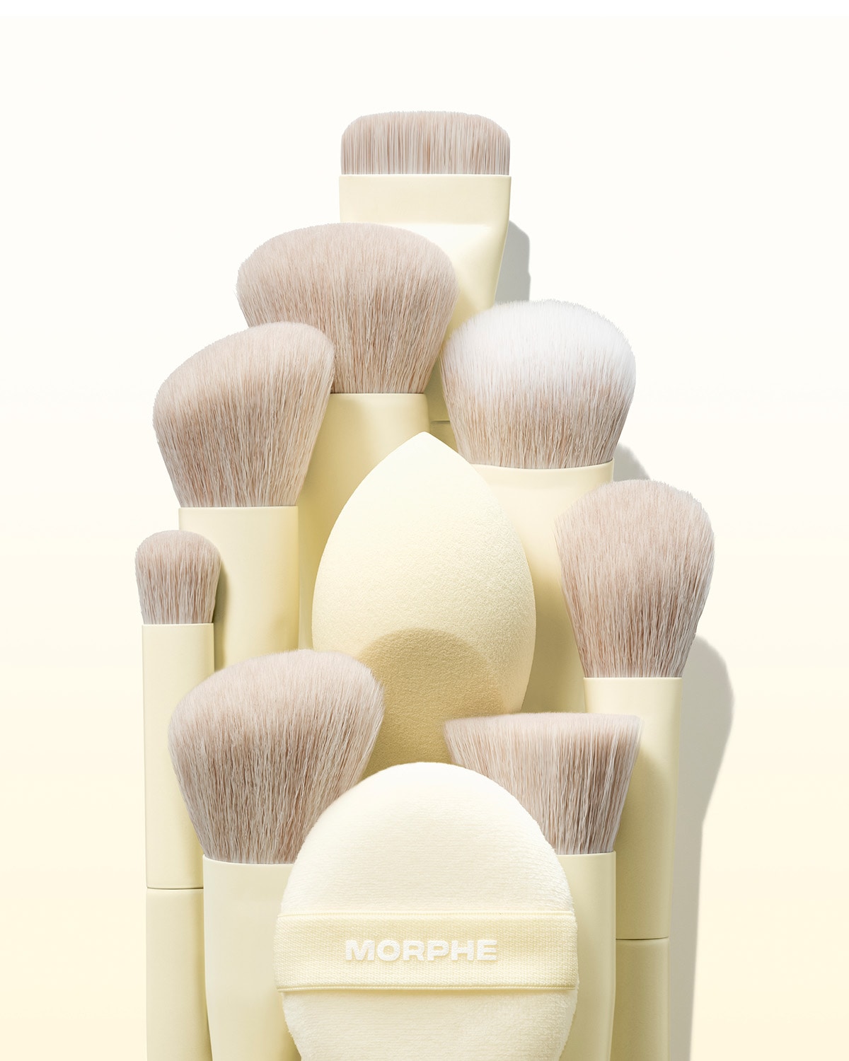 Súprava štetcov Morphe v odtieňoch slonovinovej kosti s rôznymi veľkosťami štetín a okrúhlym púdrom s logom Morphe.
