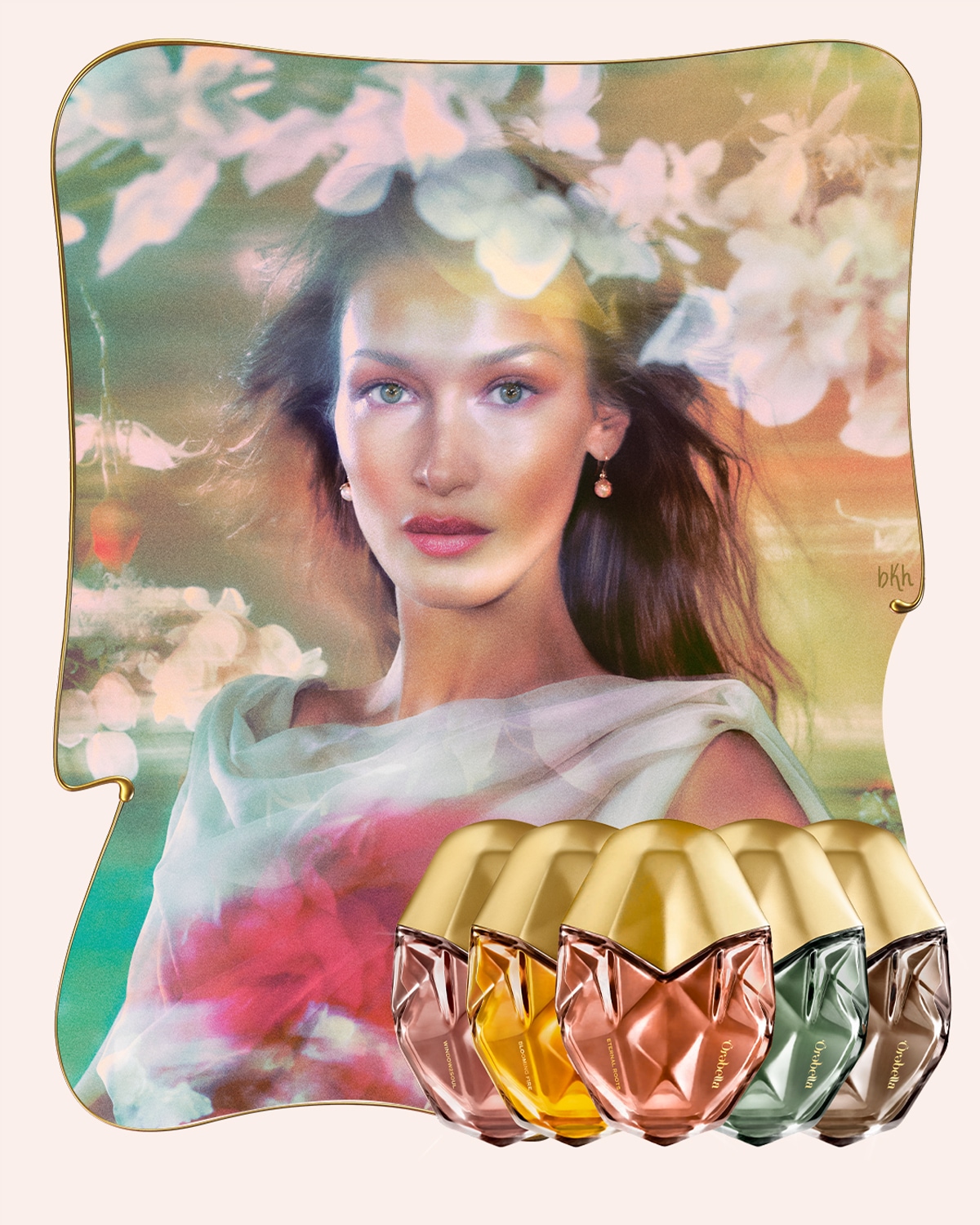 Na obrázku je modelka Bella Hadid s kvetinovým vencom a šatkou, v popredí je päť flakónov parfumu Orabella s vrchnákmi zlatej farby a rôznymi odtieňmi.
