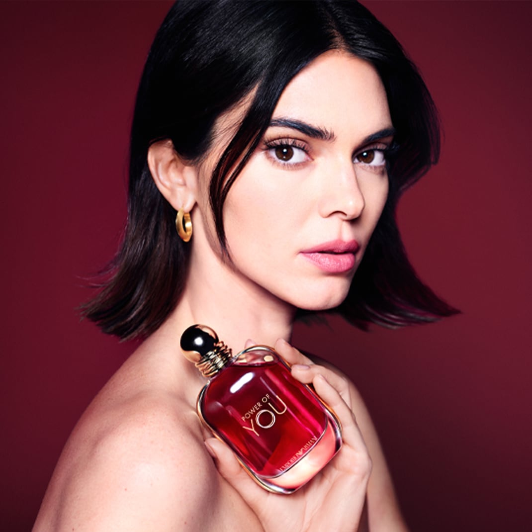 Na portréte je modelka s hnedými očami a tmavými vlasmi, ktorá drží v ruke flakón parfému Power of You s červeným nádychom a zlatým uzáverom.