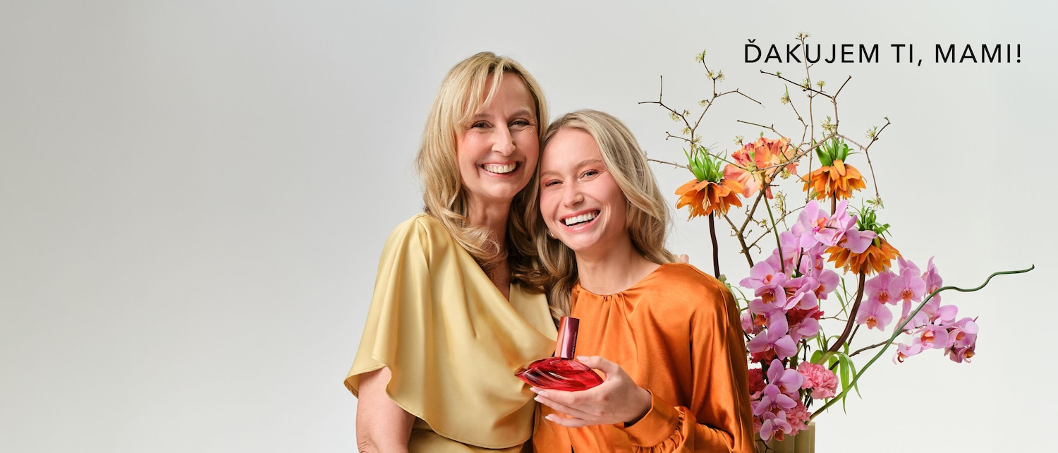 Two smiling women, one in gold and the other in orange, pose with a red perfume bottle next to a vibrant floral arrangement, with the text "Ďakujem ti, mami!"