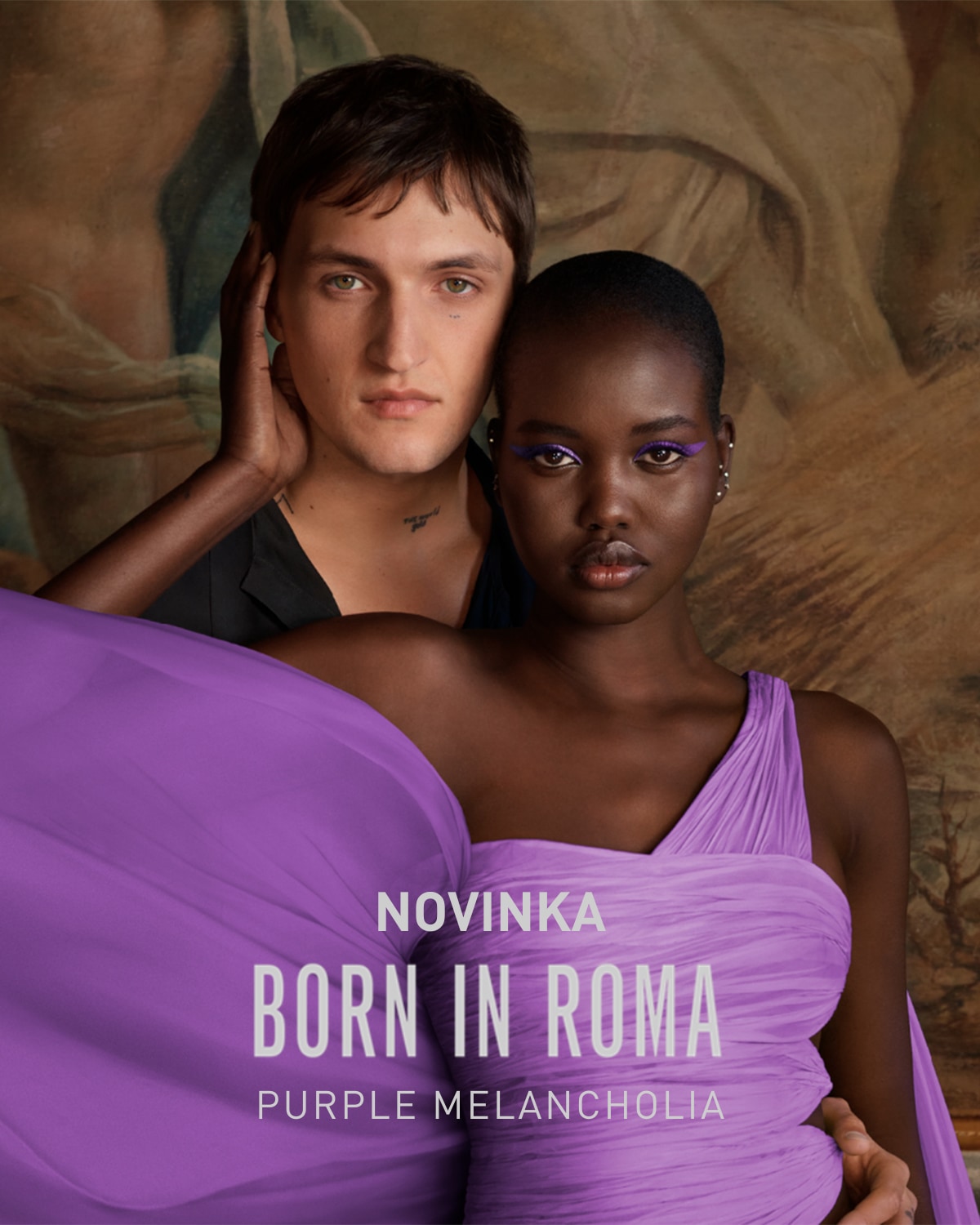 Na obrázku sú dvaja ľudia, žena s fialovými očnými linkami a muž, obaja pózujú s fialovou látkou s nápisom "NOVINKA BORN IN ROMA PURPLE MELANCHOLIA".