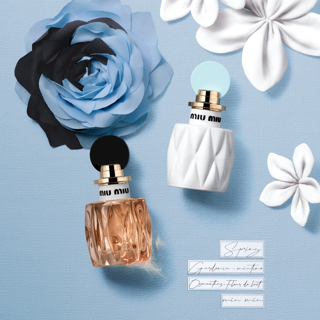 Dva flakóny parfumov Miu Miu sú obklopené kvetmi na svetlomodrom pozadí, jeden flakón je biely s textúrou a svetlomodrým vrchnákom, druhý je jantárovo sfarbený s čiernym vrchnákom.